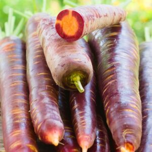 stack of purple carrots with one cut open with an orange centre