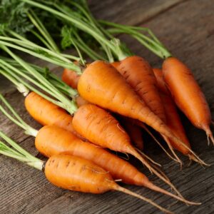 bunch of small orange carrots with long stems on a wooden table