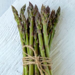 Bunched asparagus spears bound by tied string on a white, wooden table
